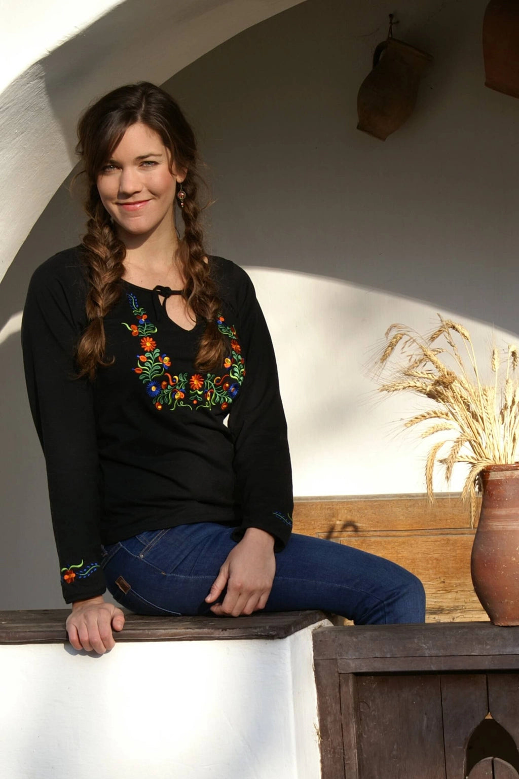 Haut noir à col fendu avec liens, inspiré de la région de Béké en Hongrie, les motifs floraux brodés sont disposés tout autour du col et sur les poignets. Vue de face, un peu en biais