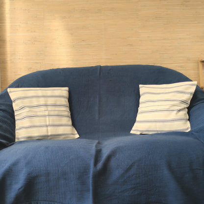 Deux coussins avec une housse tissée à la main par un artisan, 40x40cm en coton. Coloris noir et crème. Vue sur canapé.