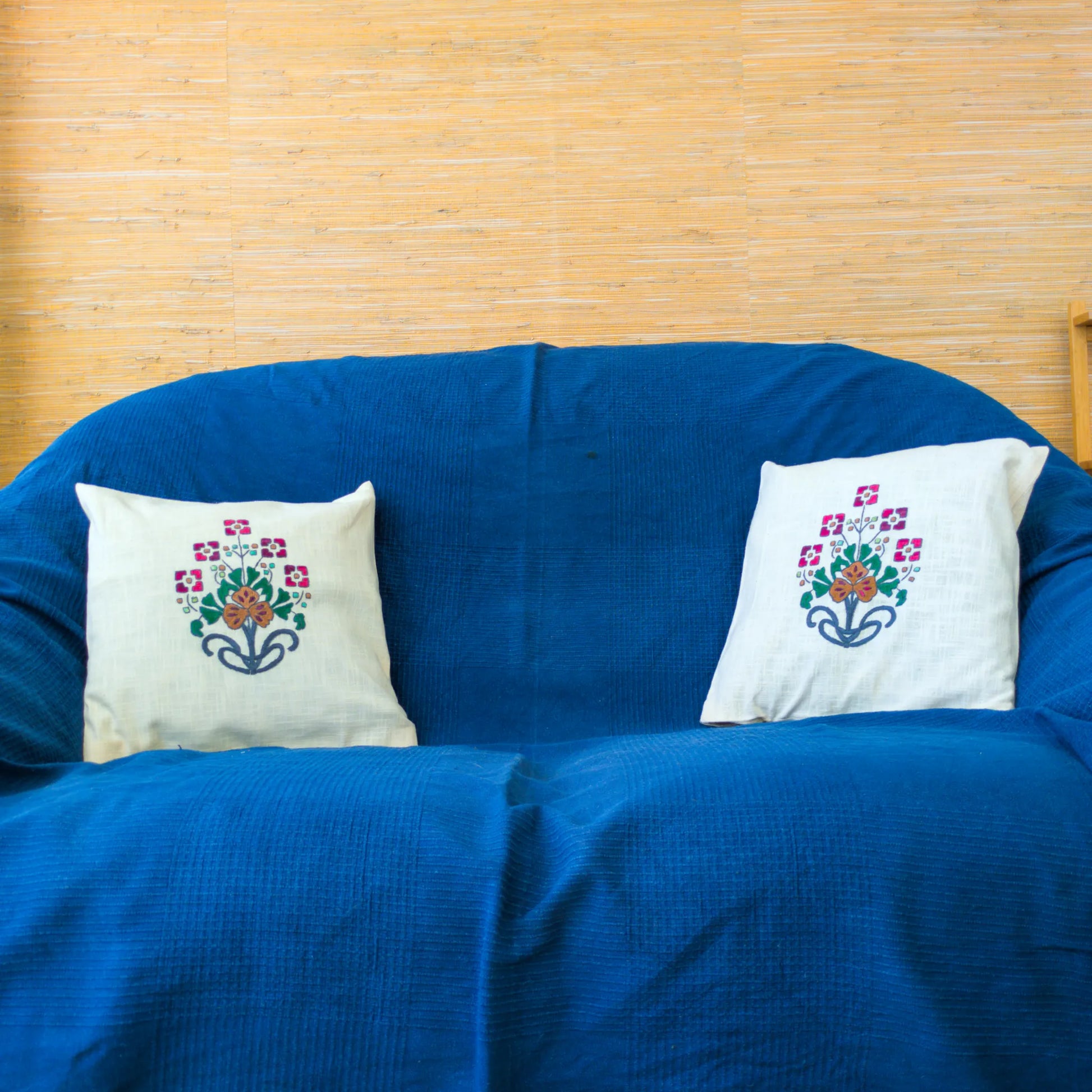 Canapé décoré de deux housses de coussin en lin brodé à la main. Les fleurs rouges et la grande fleur ocre centrale créent un équilibre visuel parfait.