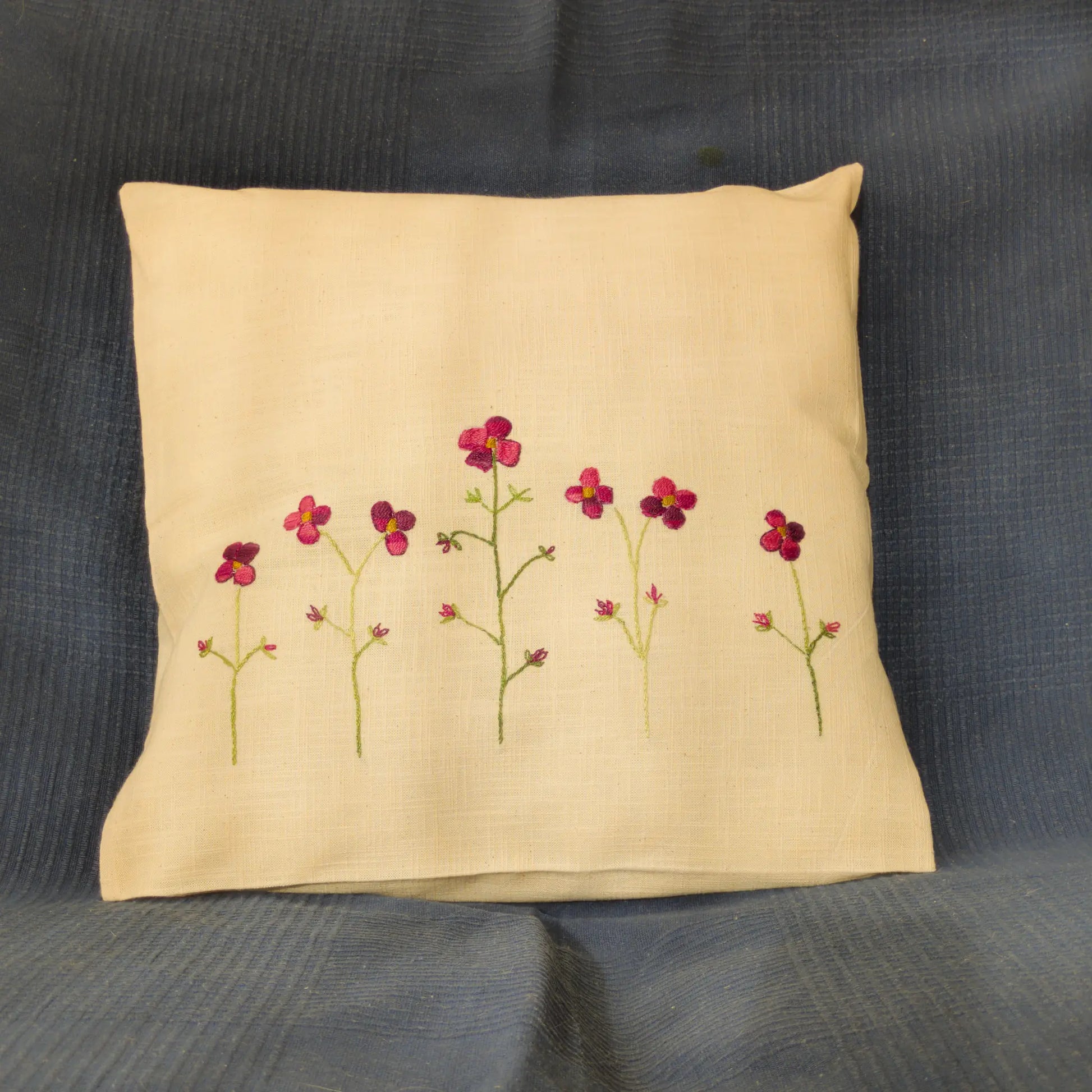 Housse de coussin en lin lavé brodée de coquelicots stylisés. Les fleurs rouges se dressent sur des tiges fines. Un motif floral léger et élégant.