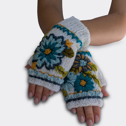 Mitaines blanc cassé portées mains croisées, avec fleurs bleues et turquoises crochetées et broderies végétales.