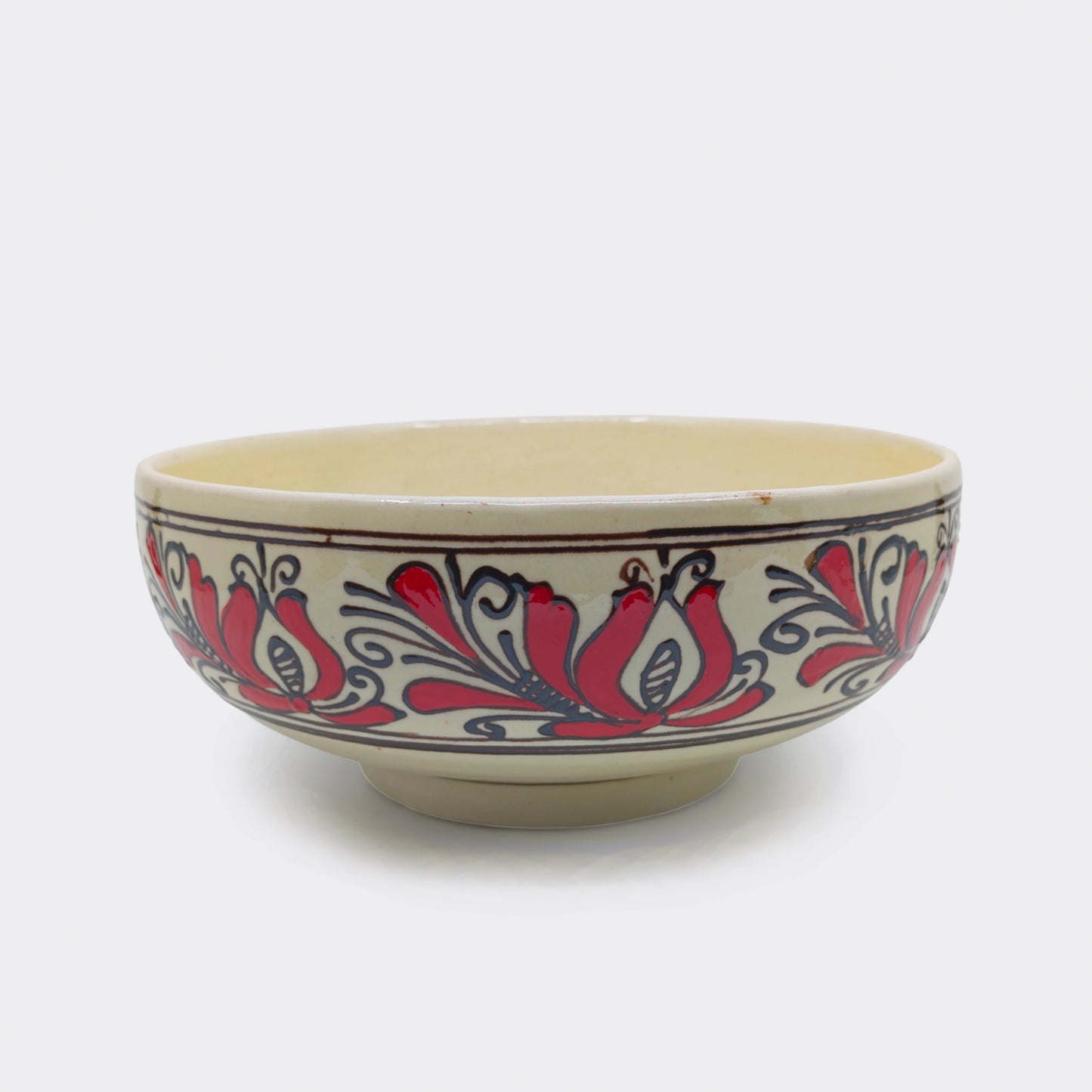 Jatte en céramique artisanale de Transylvanie avec décor floral rouge et brun. Les motifs populaires sont peints à la main sur fond crème. Cette jatte de Corund peut accueillir fruits, salades ou mets de table.