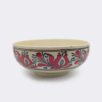 Jatte en céramique artisanale de Transylvanie avec décor floral rouge et brun. Les motifs populaires sont peints à la main sur fond crème. Cette jatte de Corund peut accueillir fruits, salades ou mets de table.