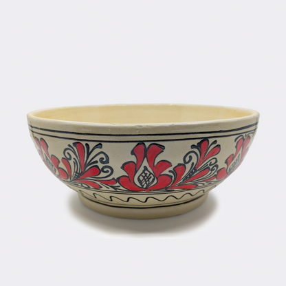 Jatte en faïence artisanale de Corund décorée à la main de motifs floraux rouges sur fond crème. Une frise simple apparaît au pied de la pièce.