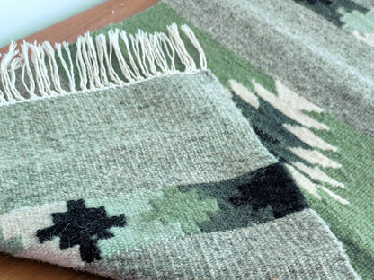 Kilim réversible vert olive et gris, replié pour montrer l’endroit et l’envers du tissage