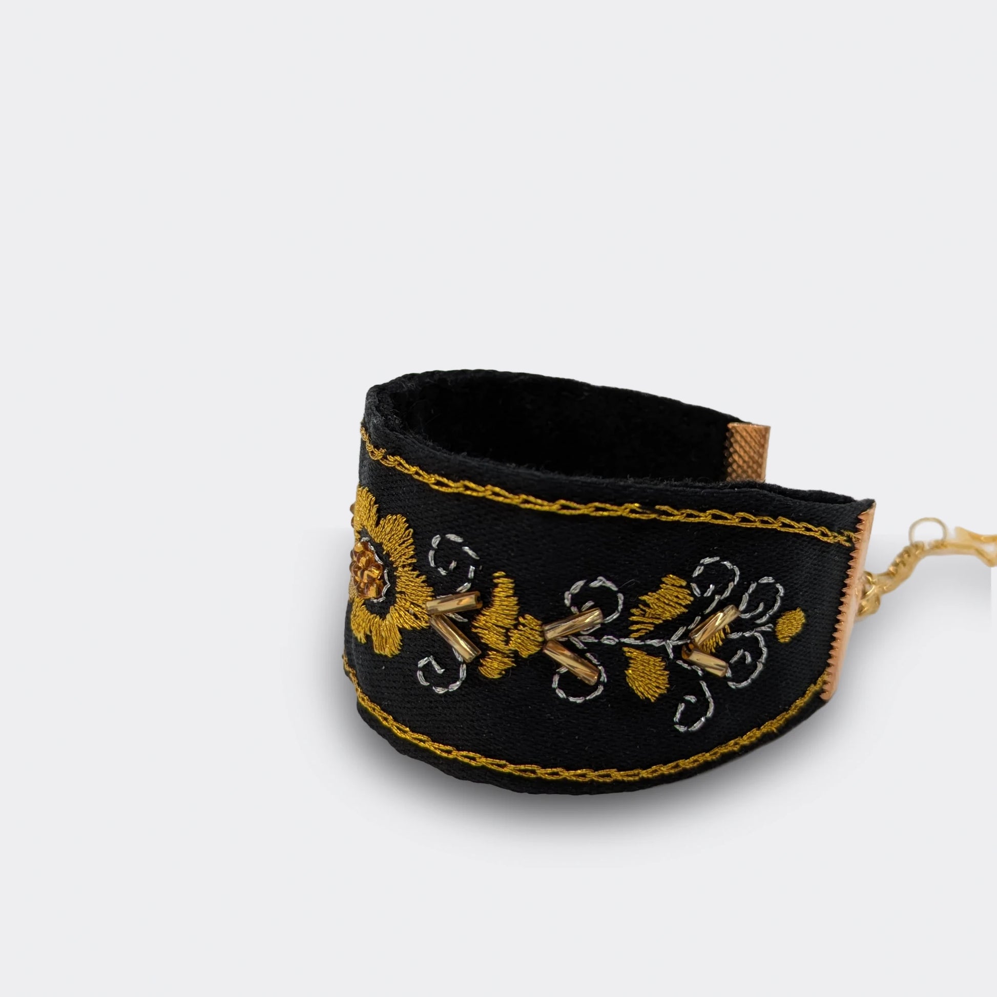 Motif floral doré au cœur d’une manchette noire brodée à la main. Exemple de broderie traditionnelle balkanique, réalisée en fils métalliques, vue rapprochée.