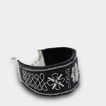 Gros plan sur la broderie argentée d’un bracelet textile noir, ornée de lignes et volutes en points traditionnels. Fait main en Serbie, détail du motif.