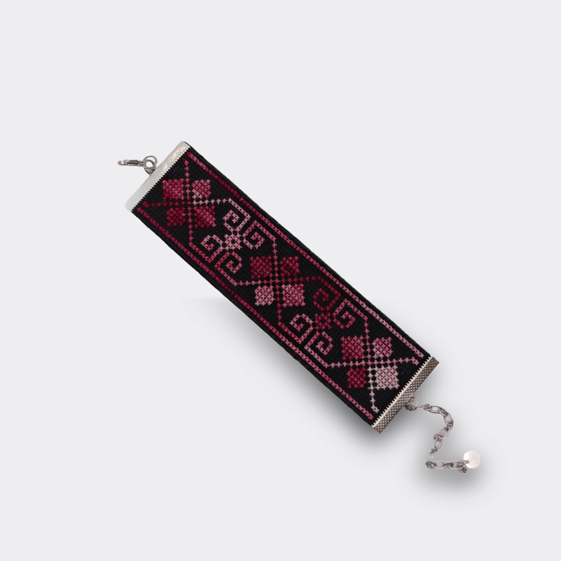 Bracelet manchette artisanal en toile Panama brodé manuellement. Motifs géométriques en rose grenat sur fond noir