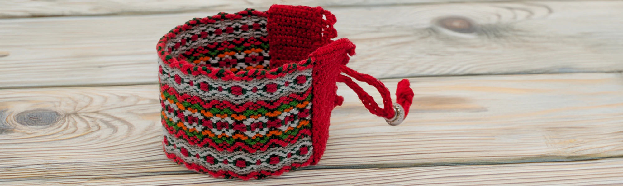 gros plan d'une manchette tissée de couleur rouge et blanche principalement. Posée sur une table en bois blanchi.