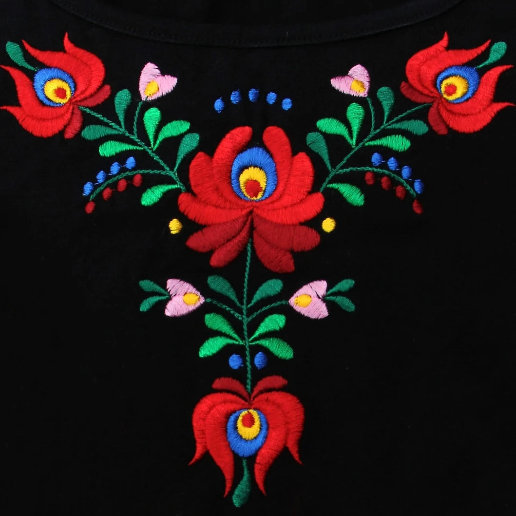 Zoom sur la broderie florale Matyó sur ce T shirt à manches courtes. Le rouge des grandes fleurs est éclatant et la forme évocatrice de traditions encore ancrées dans la Hongrie d'aujourd'hui.