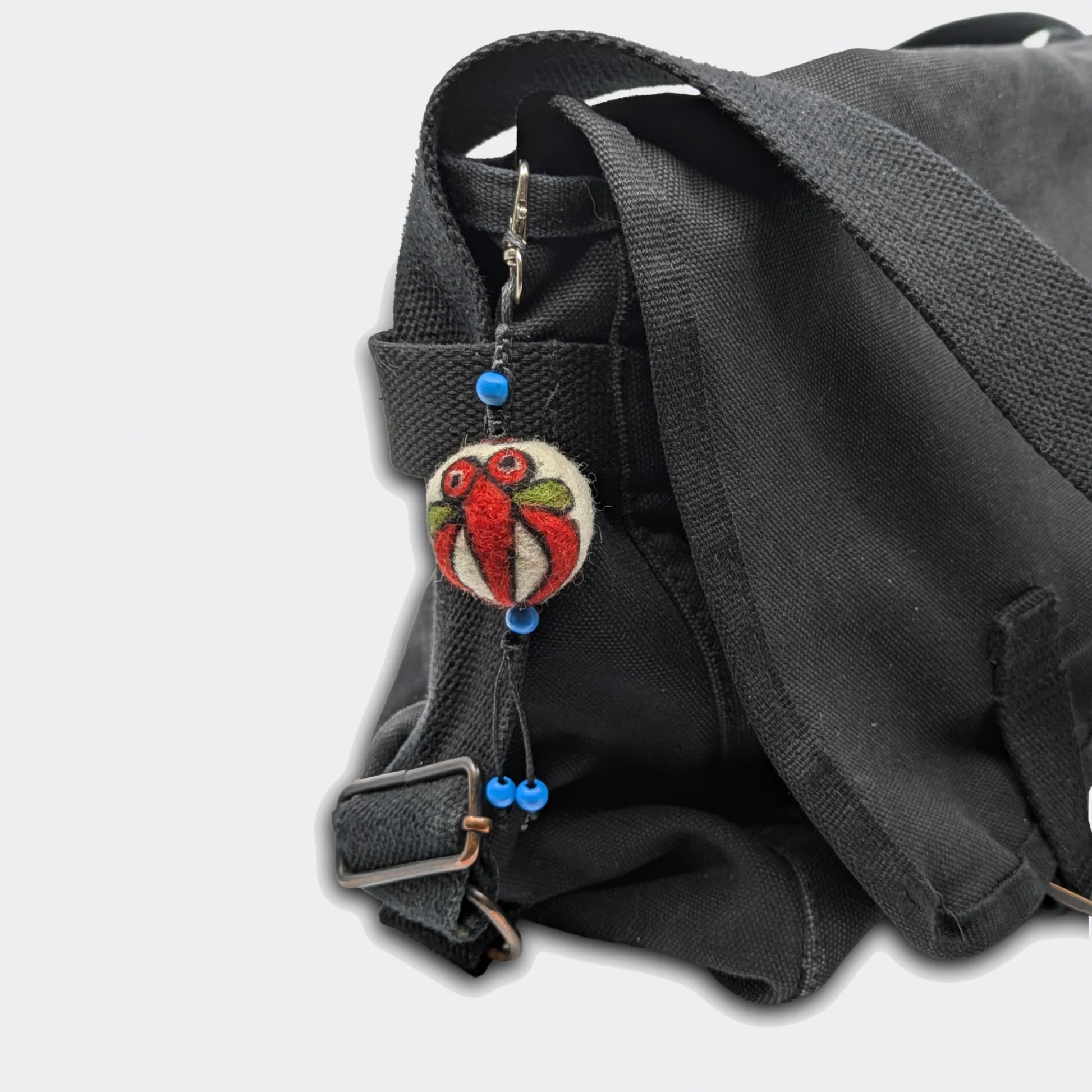Breloque Milodrag accrochée sur sac, motif stylisé rouge sur une petite boule en feutre artisanale