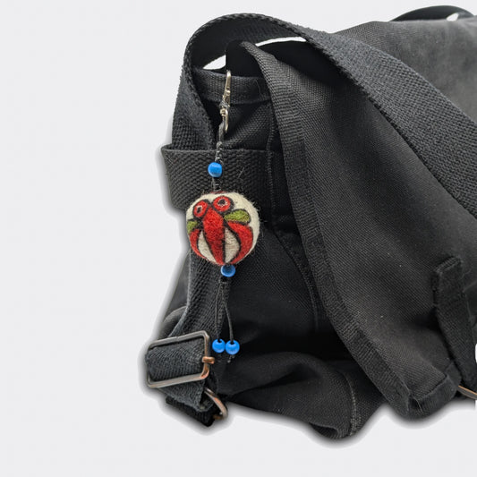 Breloque Milodrag accrochée sur sac, motif stylisé rouge sur une petite boule en feutre artisanale