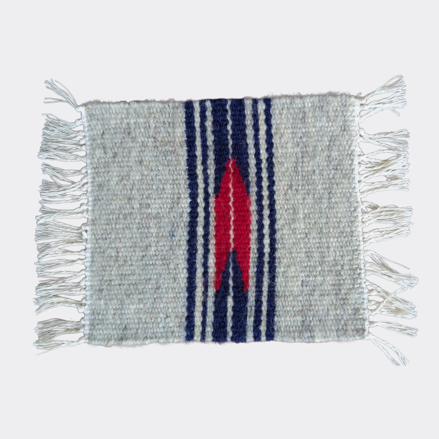 Mini tapis gris et blanc cassé traversé de bandes bleu marine et d’un motif rouge central. Tissé à la main dans un style balkanique. Un petit textile parfait pour console ou étagère.