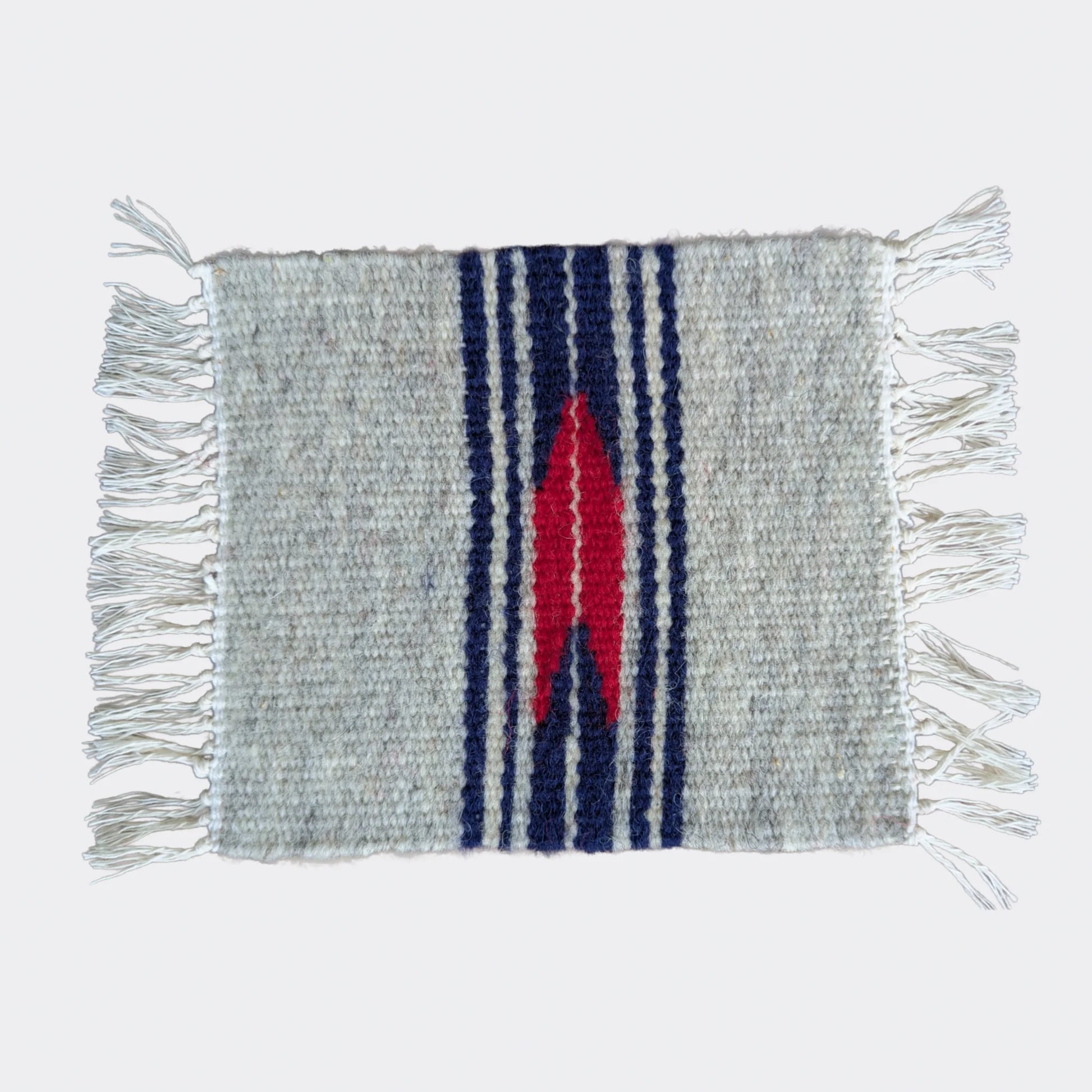 Mini tapis gris et blanc cassé traversé de bandes bleu marine et d’un motif rouge central. Tissé à la main dans un style balkanique. Un petit textile parfait pour console ou étagère.