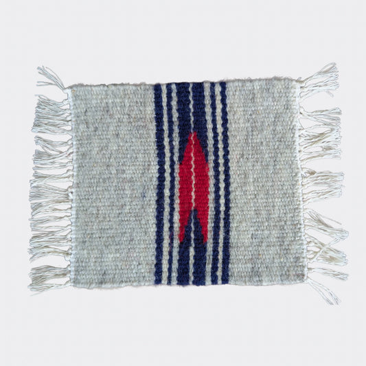 Mini tapis gris et blanc cassé traversé de bandes bleu marine et d’un motif rouge central. Tissé à la main dans un style balkanique. Un petit textile parfait pour console ou étagère.