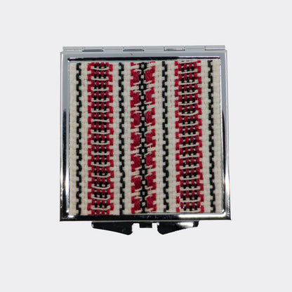Miroir compact orné d’un motif textile rouge et noir. Le décor tissé apporte une note douce venue des Carpates. Idéal pour glisser dans un sac.