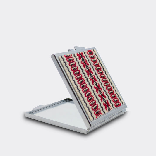 Miroir de poche décoré d’un tissu tissé rouge, noir et écru. Motif géométrique inspiré d’Europe centrale. Un petit accessoire de sac pour retouches simples.
