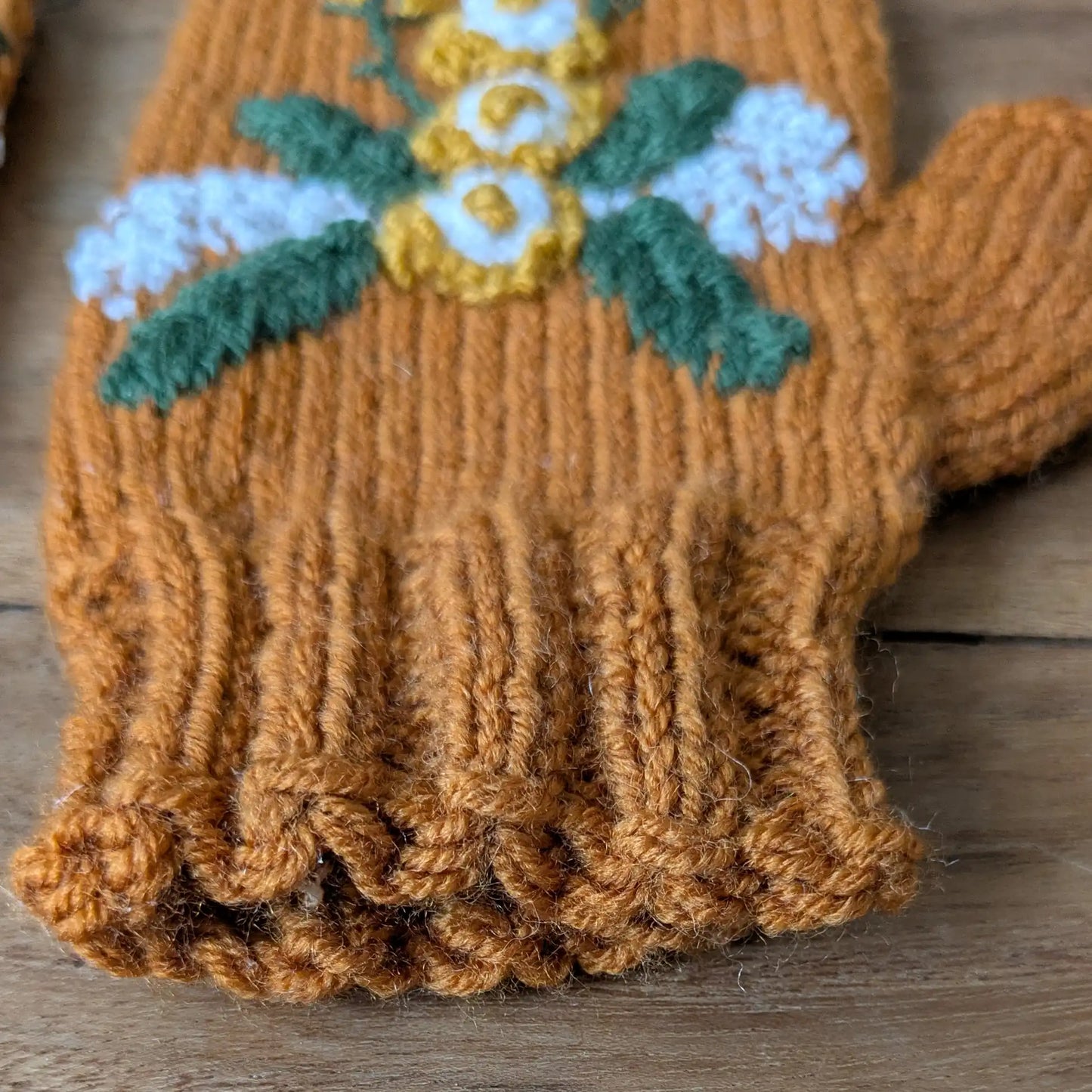 Détail du décor floral en relief avec fleurs blanches et jaunes crochetées sur des mitaines artisanales couleur cuivre. Ainsi que du bord côte.