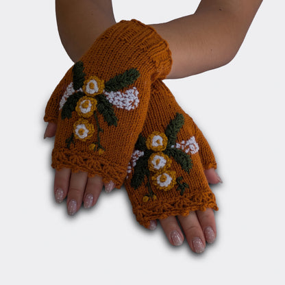 Mitaines brun cuivré portées mains croisées, tricotées main avec fleurs jaunes et blanches appliquées, feuillage vert et petites broderies blanches.