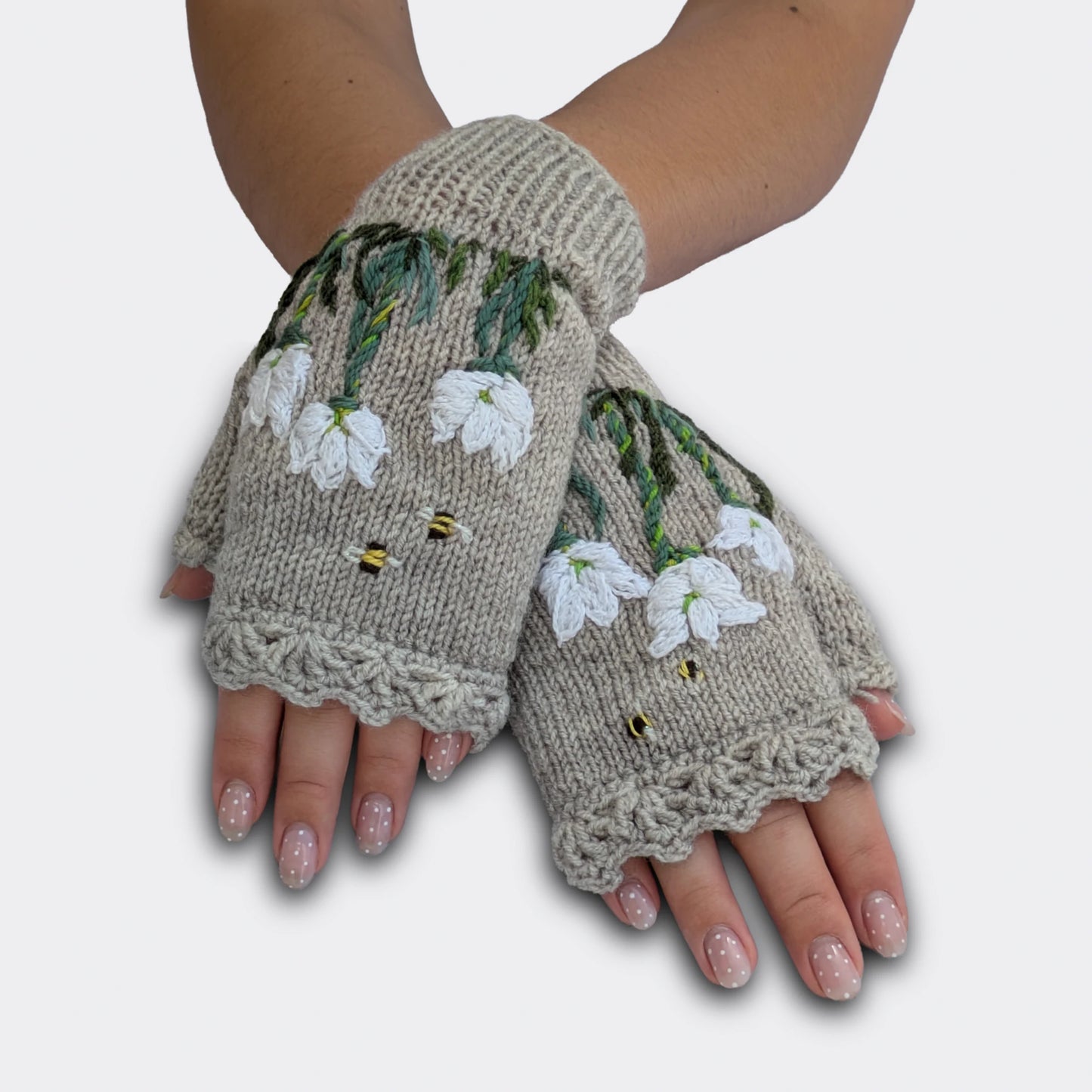 Mitaines gris perle portées mains croisées, tricotées main avec crocus blancs appliqués, broderies végétales et petites abeilles.