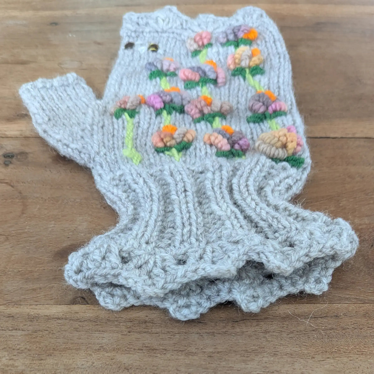 Mitaine grise faite main présentée de côté, avec ses petites fleurs multicolores sur tiges vertes. Le poignet tricoté en côtes et la bordure inférieure festonnée sont bien visibles.