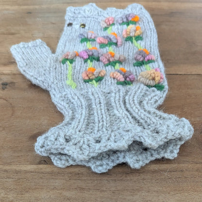 Mitaine grise faite main présentée de côté, avec ses petites fleurs multicolores sur tiges vertes. Le poignet tricoté en côtes et la bordure inférieure festonnée sont bien visibles.