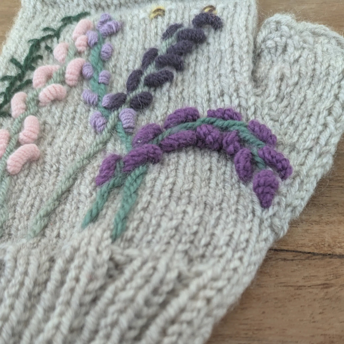 Mitaines tricotées main, maille jersey, composition florale ressemblant aux landes, couleurs parme, violet et rose pâle. Vue latérale droite, côté pouce.