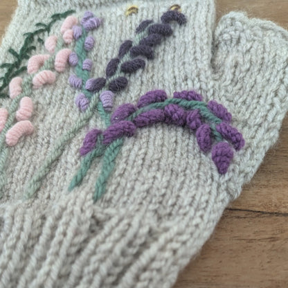 Mitaines tricotées main, maille jersey, composition florale ressemblant aux landes, couleurs parme, violet et rose pâle. Vue latérale droite, côté pouce.