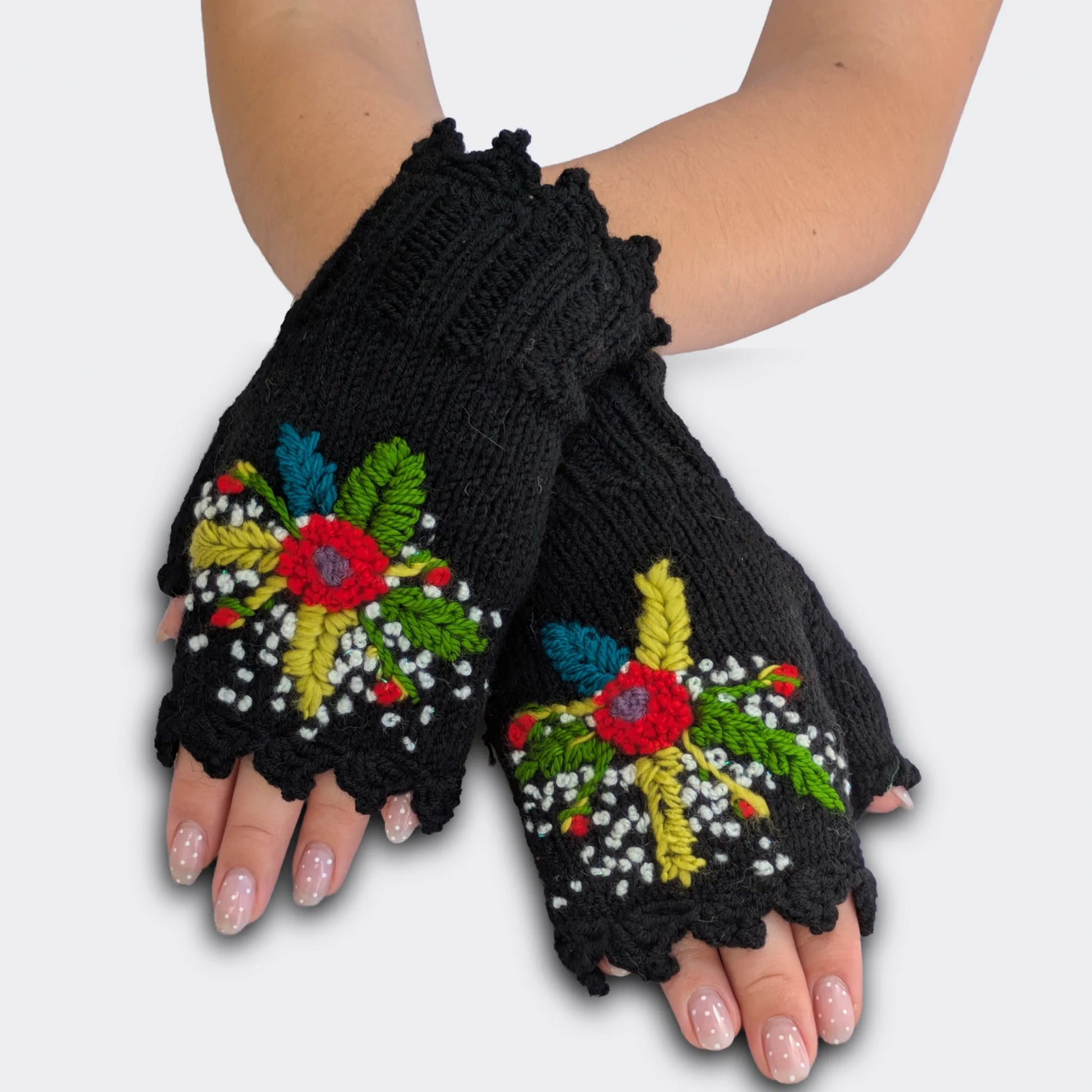 Mitaines noires portées mains croisées, tricotées main avec bouquet floral multicolore, fleurs crochetées et tiges brodées.