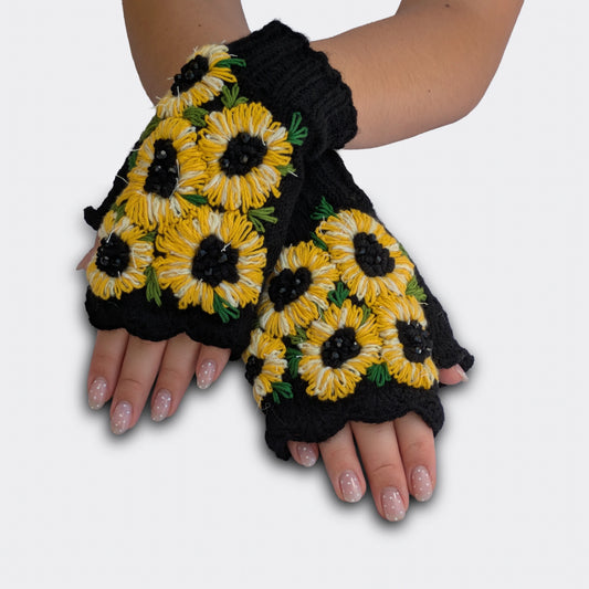 Mitaines noires portées mains croisées, tricotées main avec grands tournesols jaunes et blancs appliqués.