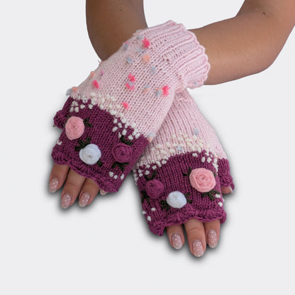 Mitaines rose clair portées mains croisées, tricotées main avec roses pastel crochetées, bord vieux rose et feuillage brodé.