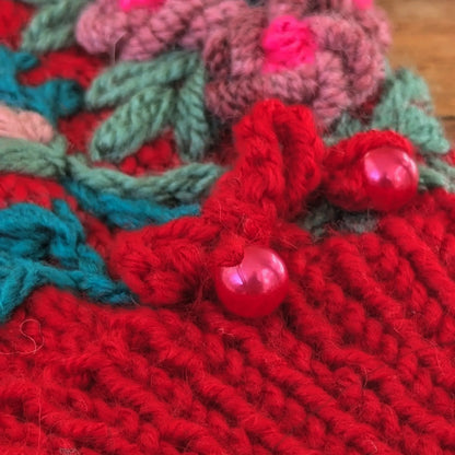 Zoom sur mitaines femme rouges tricotées, on y voit le bord côte et deux petites perles nacrées en guise de décoration