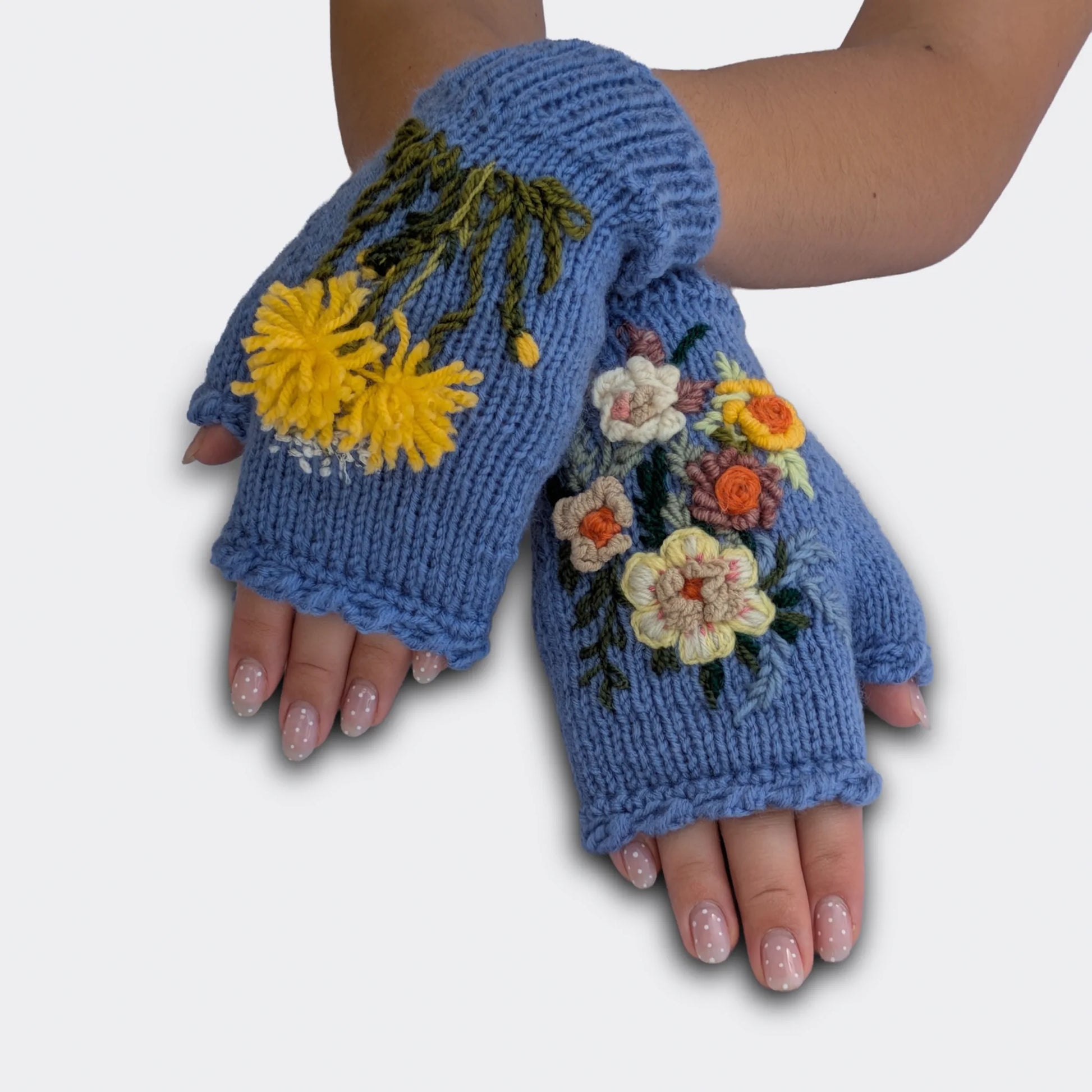 Mitaines bleu lavande portées mains croisées, avec grand pissenlit jaune brodé et fleurs champêtres crème et orange.