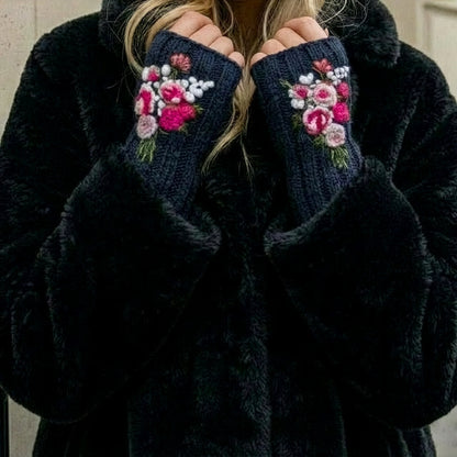 Mitaines brodées bleu nuit, portées avec un manteau noir, décorées de fleurs roses, blanches et fuchsia sur le dessus des mai
