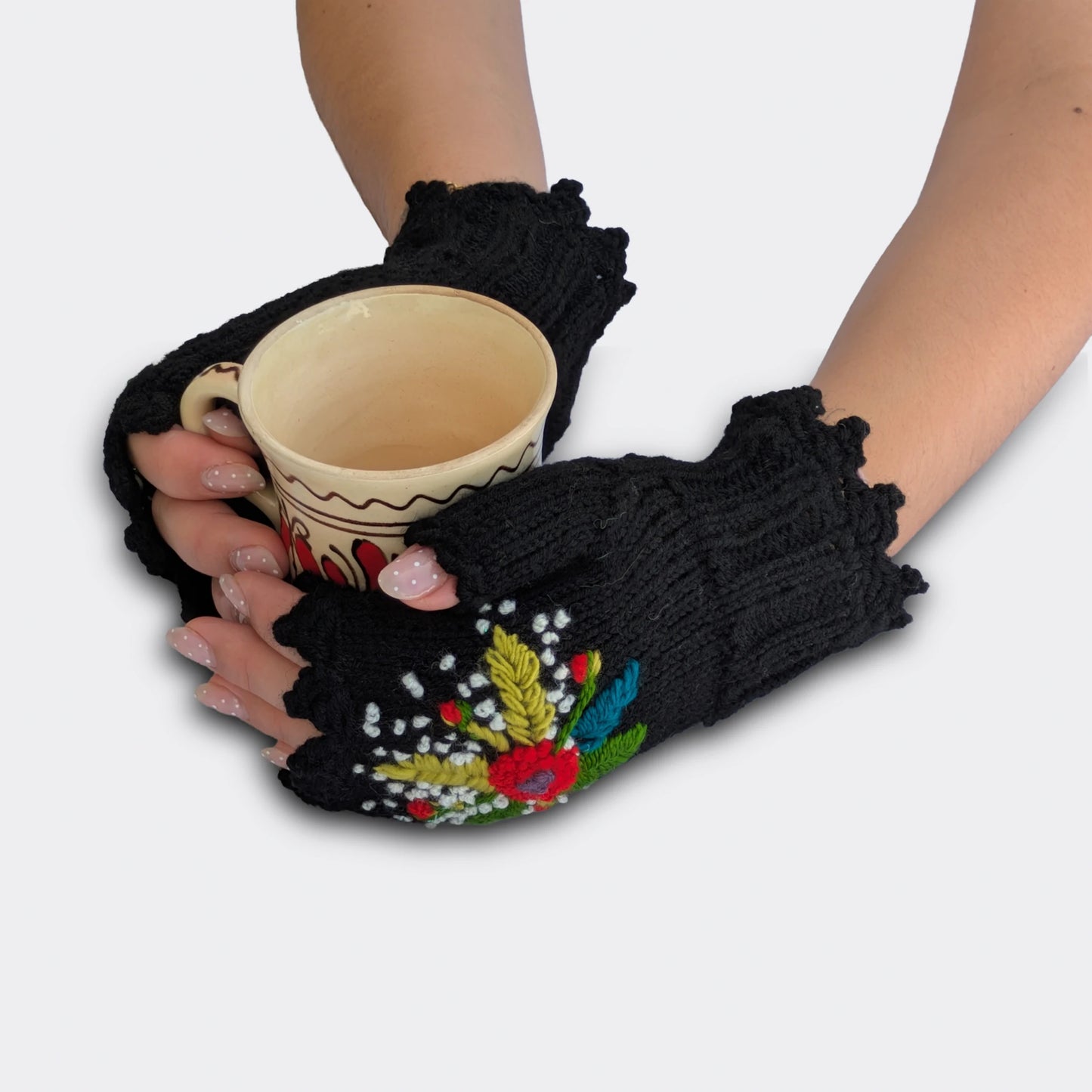 Mitaines noires tenant une tasse, décorées d’un bouquet multicolore en relief avec broderies de feuillage et tiges vertes.