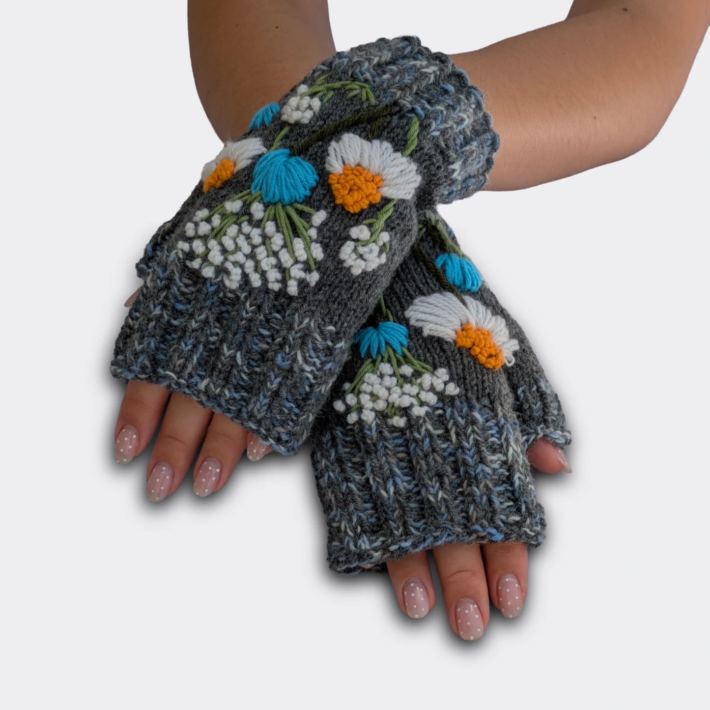 Mitaines gris chiné portées mains croisées, tricotées main et brodées de camomilles blanches à cœur jaune avec petites fleurs bleues.