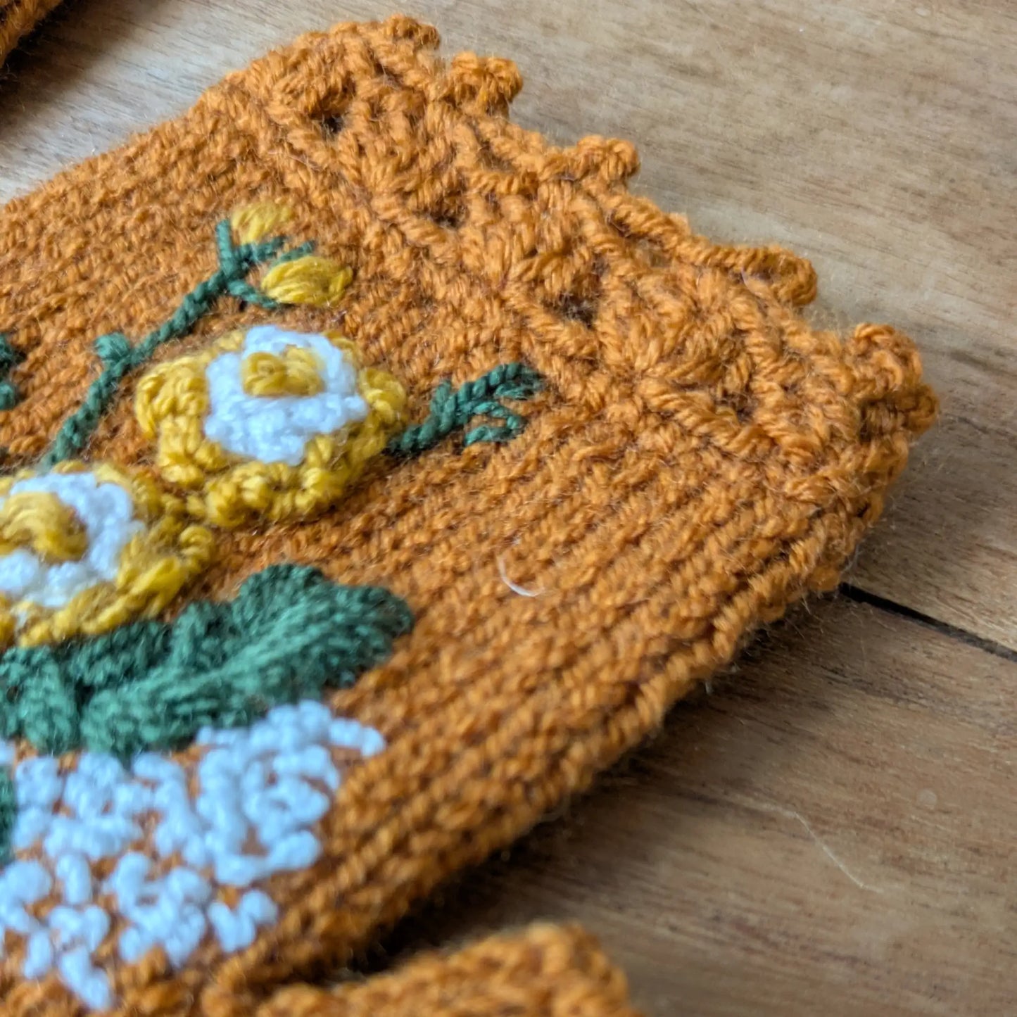 Gros plan sur le bord supérieur festonné au crochet et les fleurs appliquées sur ces mitaines couleur cuivre.