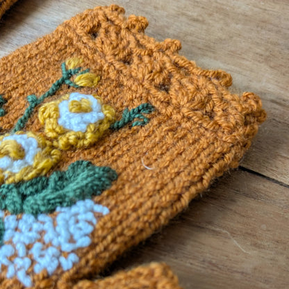 Gros plan sur le bord supérieur festonné au crochet et les fleurs appliquées sur ces mitaines couleur cuivre.