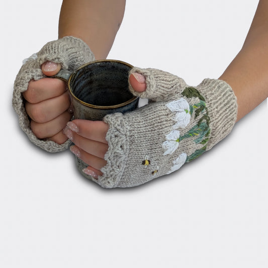Mitaines gris perle tenant une tasse, décorées de crocus blancs en relief, de tiges brodées et d’un bord côtelé.