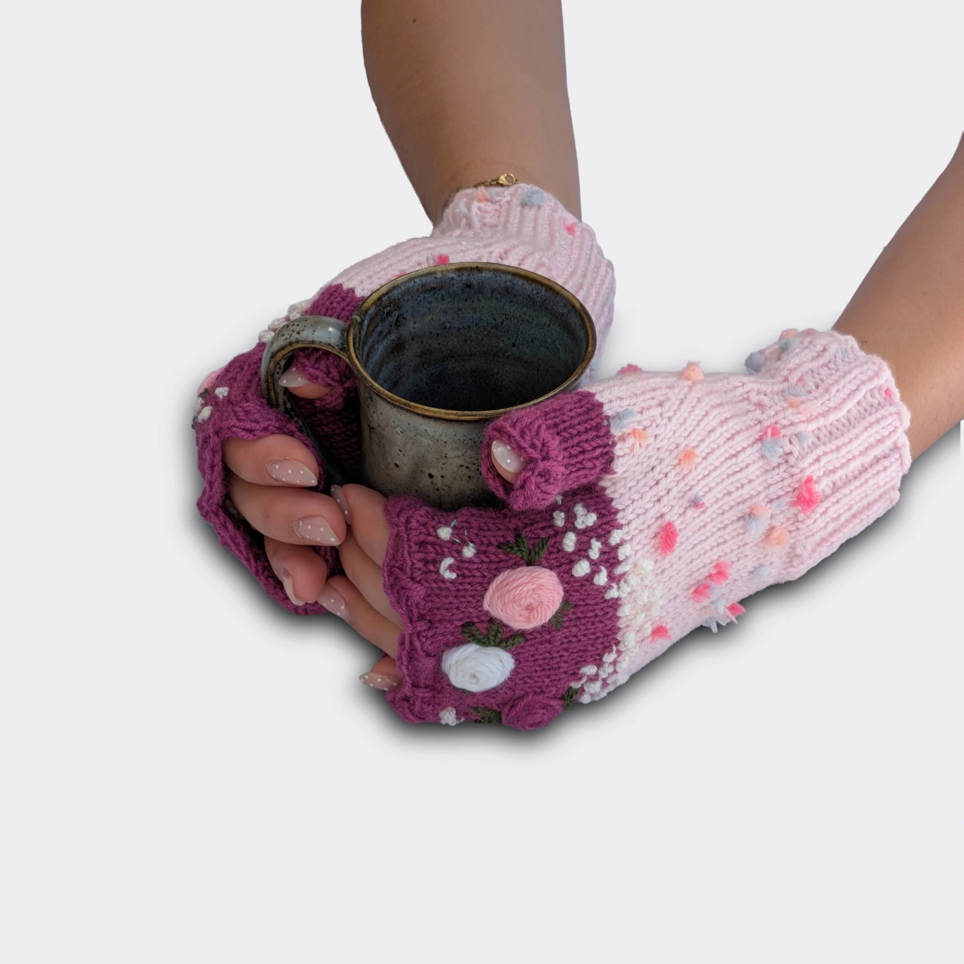 Mitaines rose clair tenant une tasse, décorées de roses pastel en relief, feuillage brodé et bord supérieur festonné.