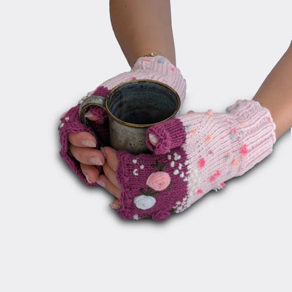 Mitaines rose clair tenant une tasse, décorées de roses pastel en relief, feuillage brodé et bord supérieur festonné.