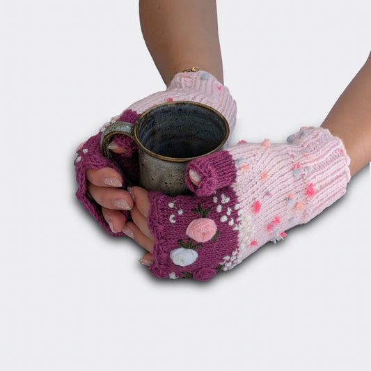 Mitaines rose clair tenant une tasse, décorées de roses pastel en relief, feuillage brodé et bord supérieur festonné.