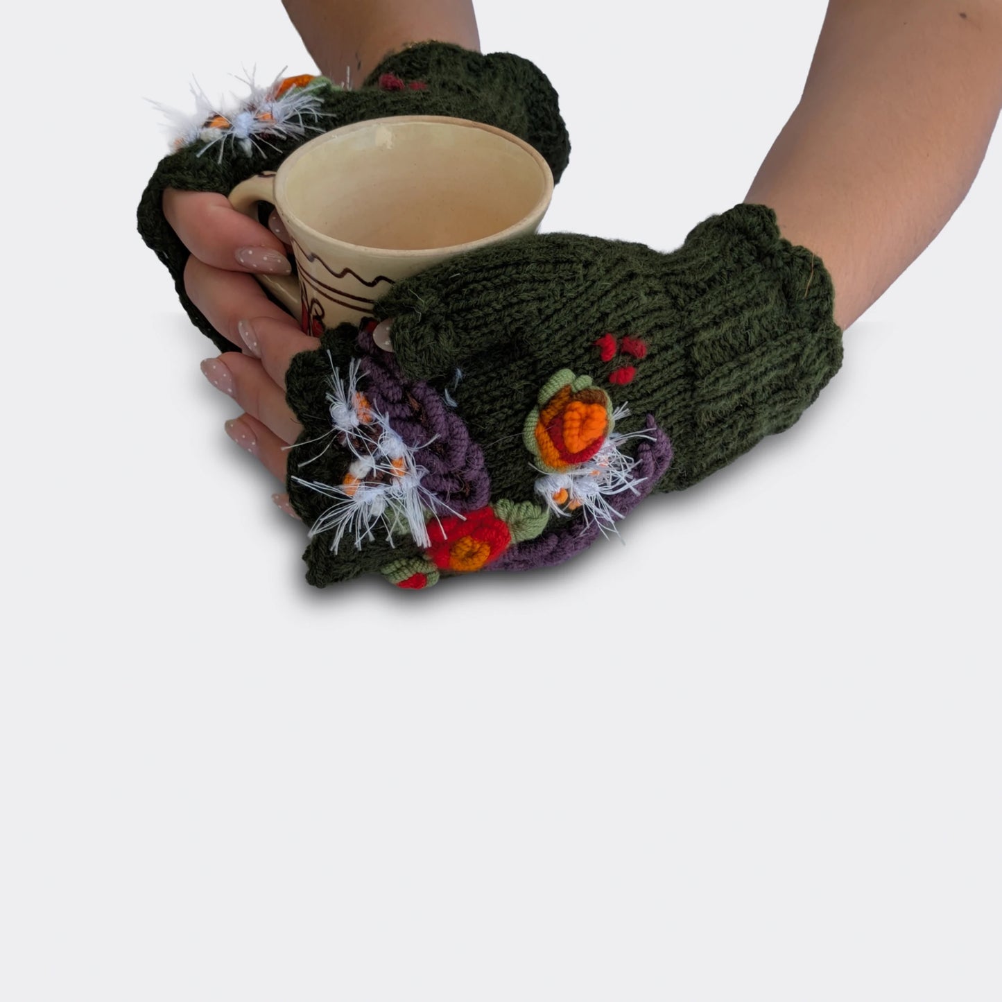 Mitaines vert olive tenant une tasse, décorées de fleurs crochetées, broderies végétales et détails floraux colorés.