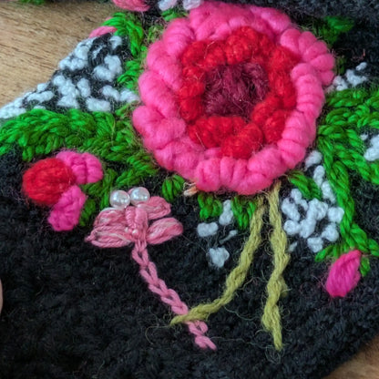 Détail de la libellule rose brodée avec petites perles nacrées sur des mitaines noires à motif floral.