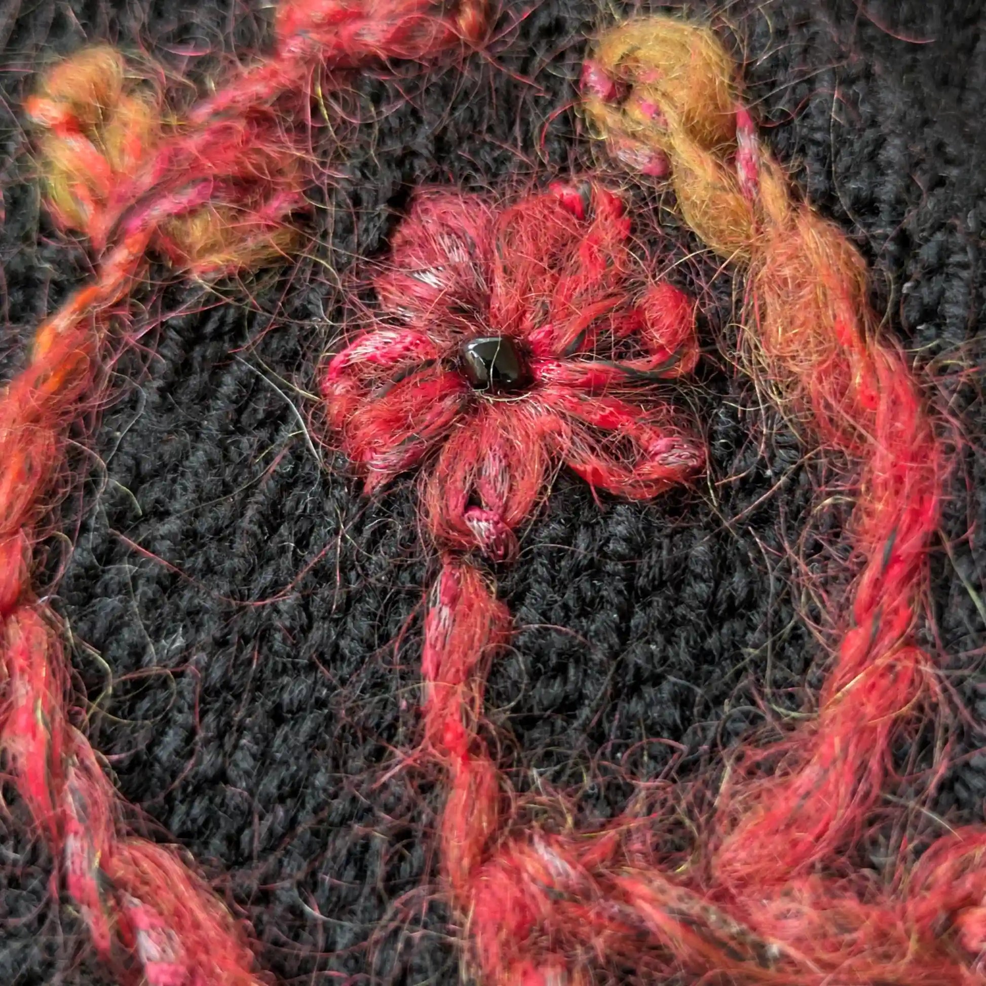 Détail du motif floral couleur rouille brodé sur la maille jersey noire des mitaines. Une perle noire figure au centre de la fleur.