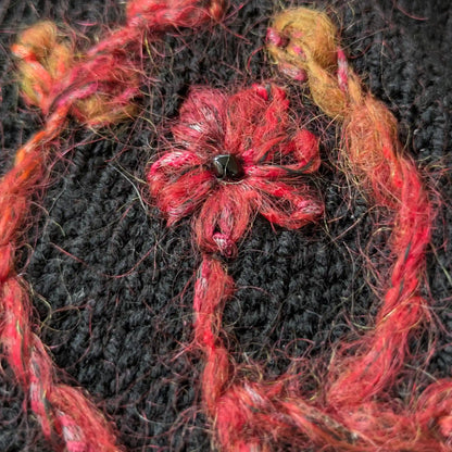 Détail du motif floral couleur rouille brodé sur la maille jersey noire des mitaines. Une perle noire figure au centre de la fleur.