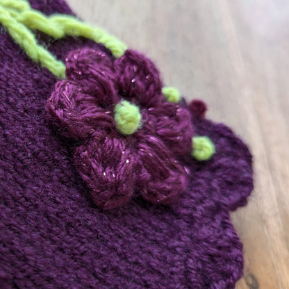Gros plan sur les fleurs violettes crochetées avec fils pailletés et petites perles vertes sur des mitaines brodées.