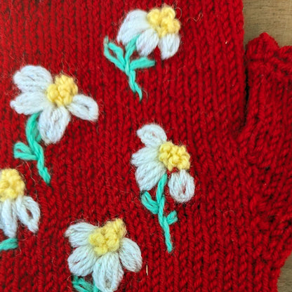 Détail de la composition florale discrète sur une paire de mitaines artisanales rouges.