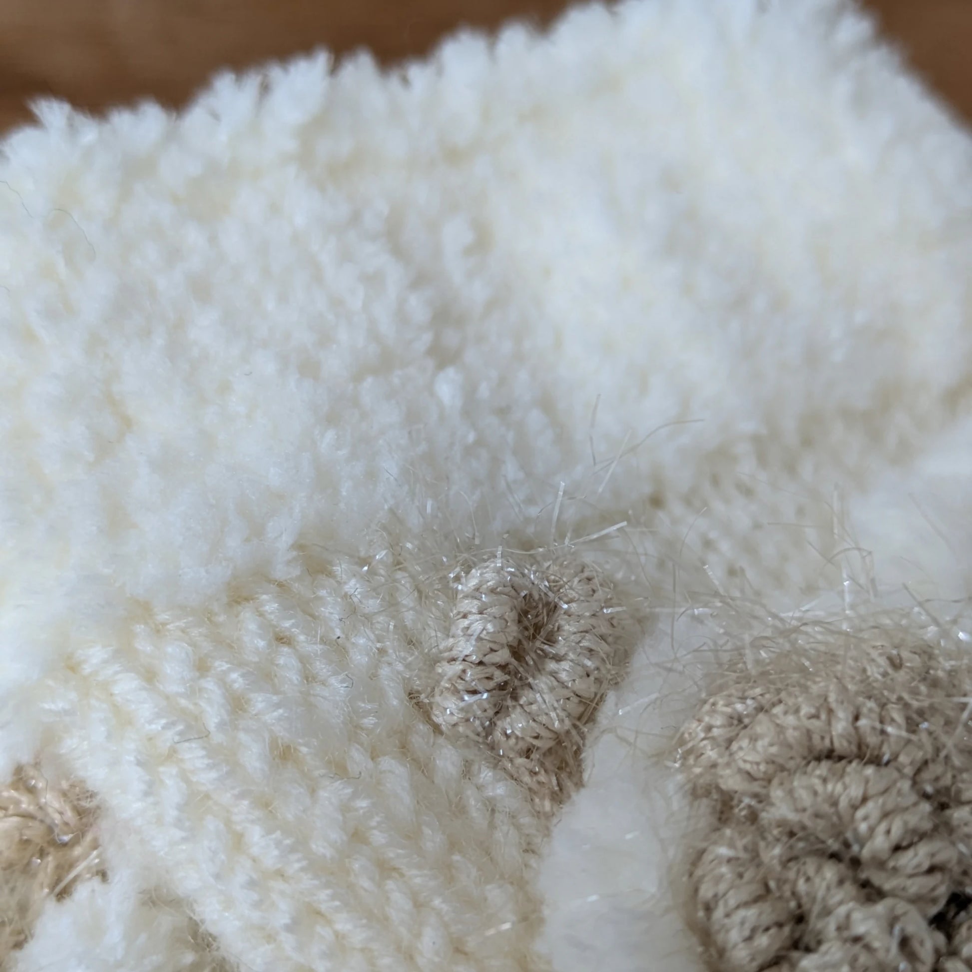 Gros plan sur la maille blanche et la fleur en relief de ces mitaines tricotées main.