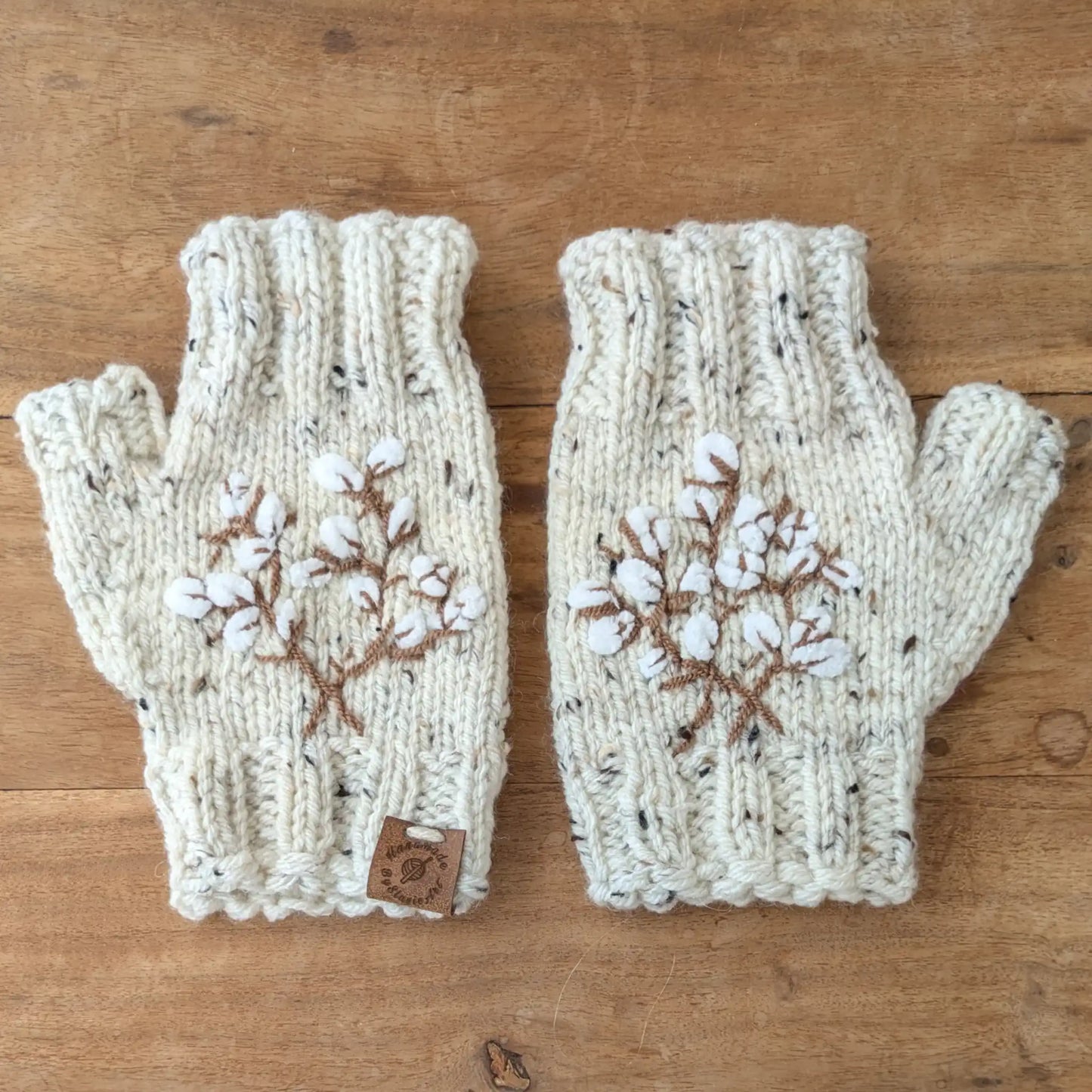 Mitaines écru moucheté faites main, avec broderies brunes en forme de branches de coton. Posées à plat.